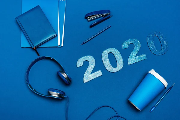 Vista superior de portátiles, auriculares, bolígrafos, grapadoras y números 2020 sobre fondo azul - foto de stock