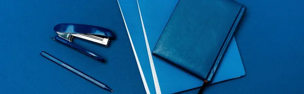 Panoramic shot of notebooks, pen and stapler isolated on blue — Stock Photo