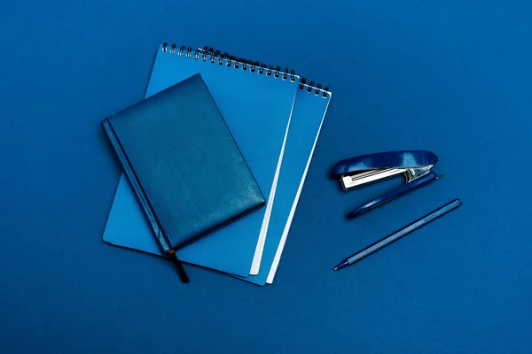 Vista superior de cuadernos, bolígrafo y grapadora aislados en azul — Stock Photo
