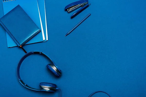 Top view of notebooks, headphones, pen, stapler on blue background — Stock Photo