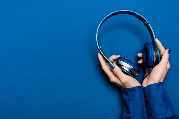 Vista cortada de mulher segurando fones de ouvido no fundo azul — Fotografia de Stock