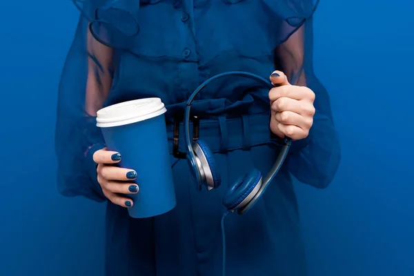 Обрезанный вид женщины с бумажной чашкой и наушниками на синем фоне — стоковое фото