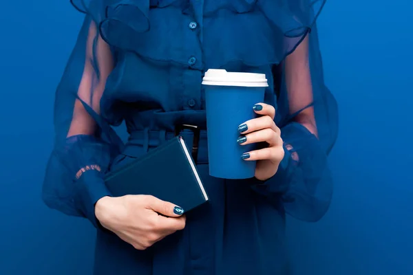 Cropped view of woman holding paper cup and notebook on blue background — Stock Photo