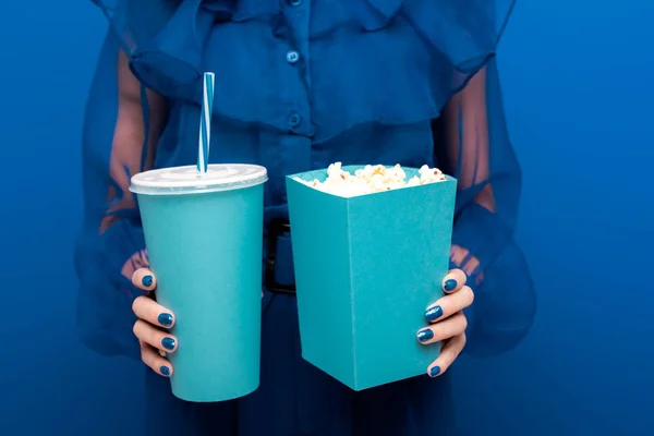 Vista recortada de la mujer sosteniendo palomitas de maíz y soda sobre fondo azul - foto de stock