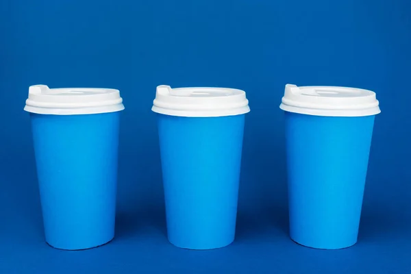 Xícaras de papel com café no fundo azul clássico — Fotografia de Stock