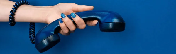 Panoramic shot of woman holding handset on blue background — Stock Photo