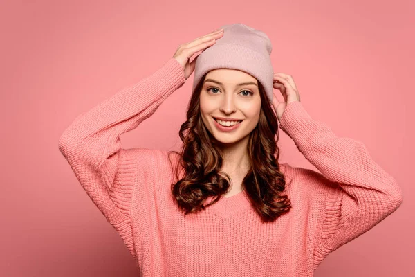 Happy girl touching hat while smiling at camera on pink background — Stock Photo