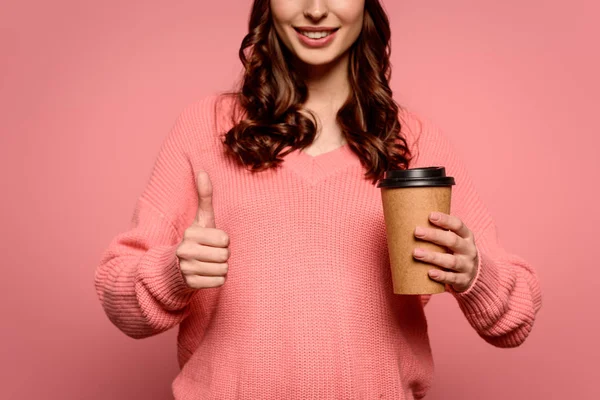 Cropped view of smiling girl holding coffee to go and showing thumb up on pink background — Stock Photo