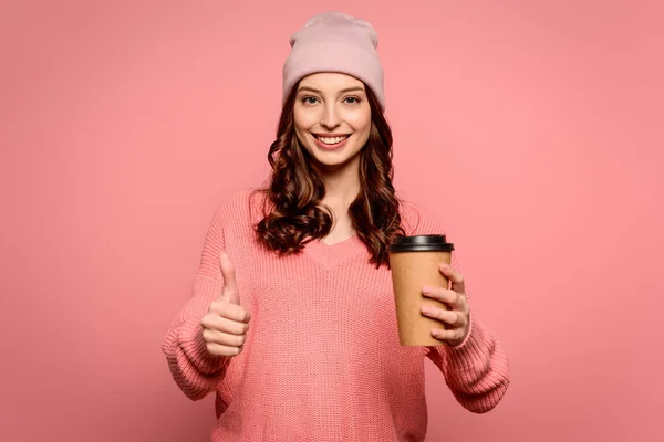 Gaie fille tenant café pour aller et montrant pouce vers le haut sur fond rose — Photo de stock