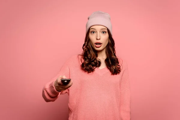 Shocked girl holding tv remote controller on pink background — Stock Photo