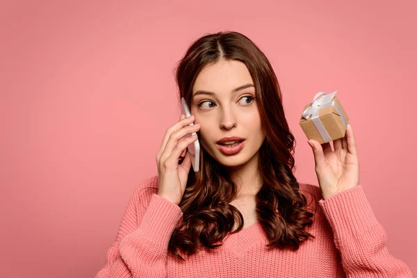 Fille surprise parlant sur smartphone et regardant boîte cadeau isolé sur rose — Photo de stock