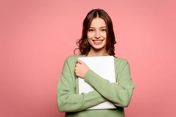 Estudiante sonriente sosteniendo portátil cerrado mientras mira la cámara aislada en rosa - foto de stock