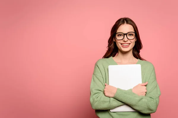 Happy businesswoman in glasses holding closed laptop while smiling at camera on pink background — Stock Photo