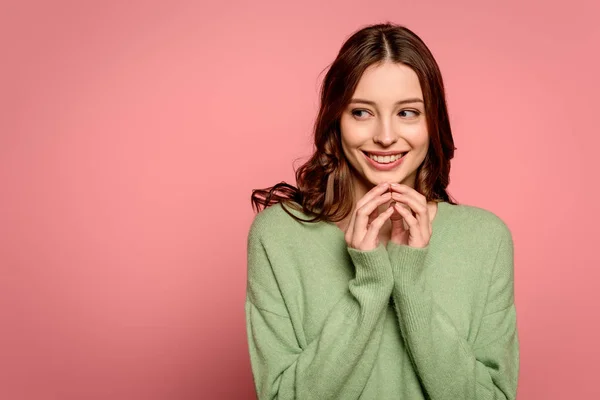 Neugieriges Mädchen schaut weg, während es die zusammengefalteten Finger in der Nähe des Gesichts auf rosa Hintergrund hält — Stockfoto