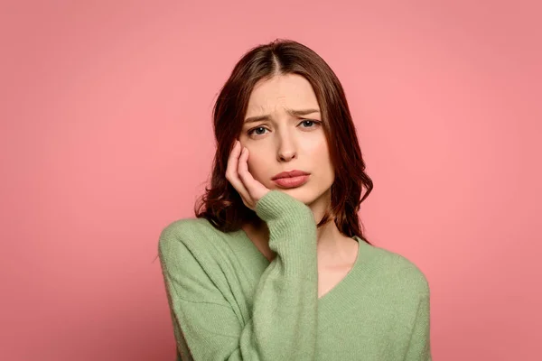 Upset girl looking at camera while touching face isolated on pink — Stock Photo