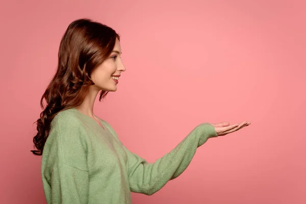 Side view of cheerful girl standing with open arm isolated on pink — Stock Photo