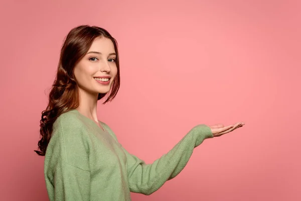 Fröhliches Mädchen lächelt in die Kamera, während es mit offenem Arm isoliert auf rosa steht — Stockfoto