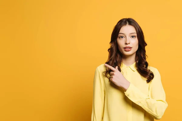 Grave, attraente ragazza guardando la fotocamera e puntando con il dito su sfondo giallo — Foto stock