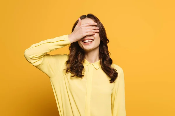 Menina sorridente cobrindo os olhos com a mão no fundo amarelo — Fotografia de Stock