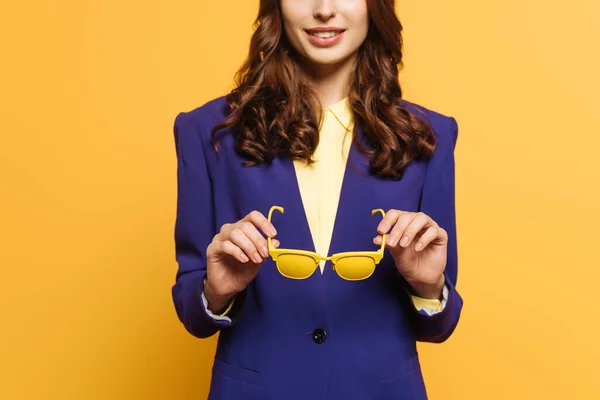 Vista cortada de menina elegante segurando óculos amarelos isolados no amarelo — Fotografia de Stock