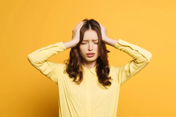 Tired girl touching hand with hands while suffering from headache with closed eyes on yellow background — Stock Photo