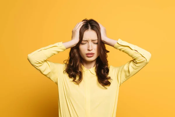 Chica cansada tocando la mano con las manos mientras sufre de dolor de cabeza con los ojos cerrados sobre fondo amarillo - foto de stock