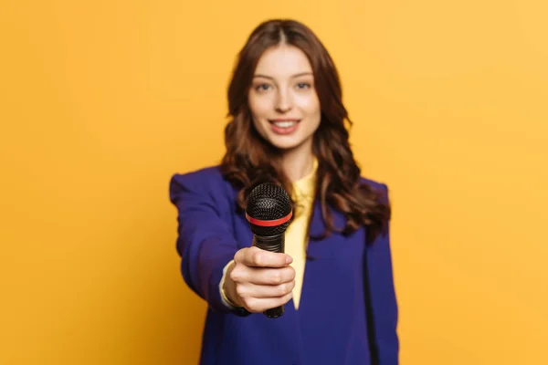 Selective focus of journalist holding microphone on yellow background — Stock Photo