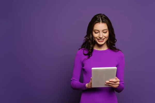 Heureuse fille souriant tout en utilisant tablette numérique sur fond violet — Photo de stock