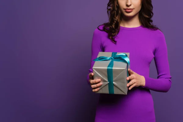 Vista recortada de la mujer joven sosteniendo caja de regalo sobre fondo púrpura - foto de stock