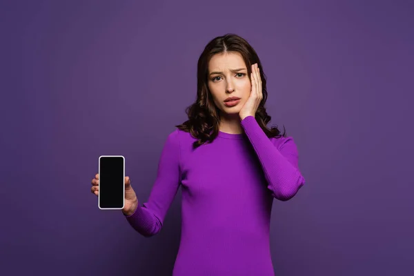 Chica molesta mostrando teléfono inteligente con pantalla en blanco sobre fondo púrpura - foto de stock