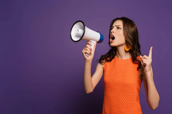 Excited girl screaming in megaphone and showing attention gesture on purple background — Stock Photo