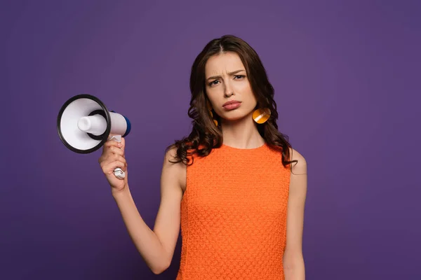 Confused girl holding megaphone and looking at camera isolated on purple — Stock Photo