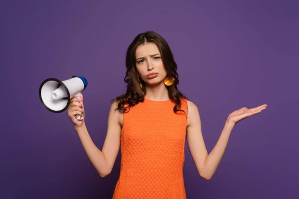 Sconvolto ragazza mostrando gesto scrollata di spalle tenendo il megafono e guardando la fotocamera isolata sul viola — Foto stock