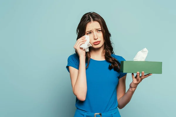 Chica triste limpiando lágrimas con servilleta de papel mientras llora aislado en azul - foto de stock