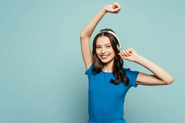 Felice ragazza che balla mentre ascolta musica in cuffie senza fili isolate sul blu — Foto stock