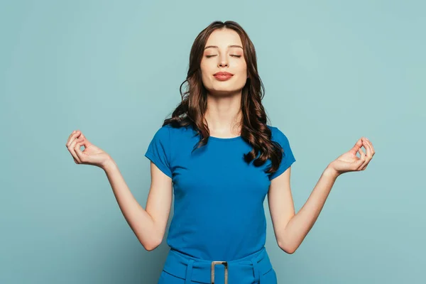 Smiling girl standing in meditation pose with closed eyes on blue background — Stock Photo
