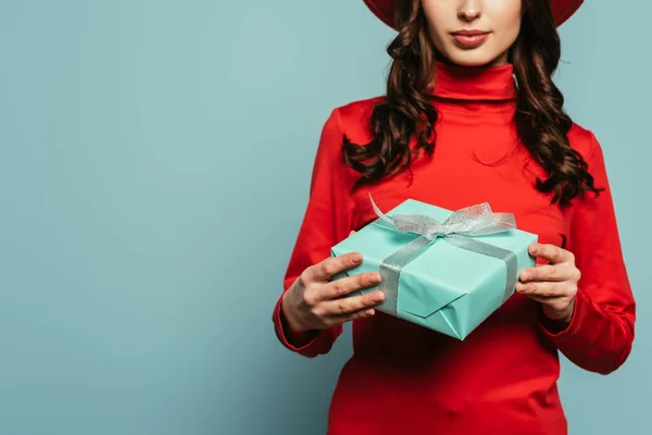 Vista recortada de la joven mujer con estilo que sostiene la caja de regalo sobre fondo azul - foto de stock