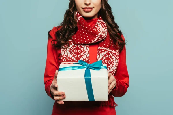 Recortado vista de chica en suéter rojo celebración caja de regalo aislado en azul - foto de stock
