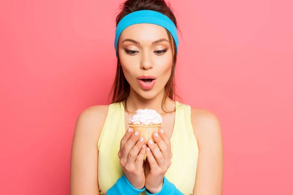 Esportista surpreso segurando delicioso cupcake no fundo rosa — Fotografia de Stock