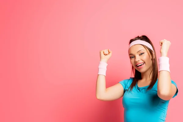 Happy sportswoman showing winner gesture while looking at camera on pink background — Stock Photo
