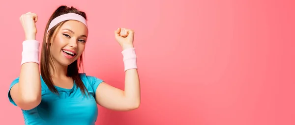 Tiro panorámico de deportista emocionada mostrando gesto ganador mientras mira a la cámara en el fondo rosa - foto de stock