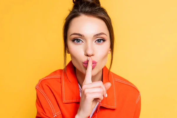 Attractive young woman showing hush gesture while looking at camera isolated on yellow — Stock Photo