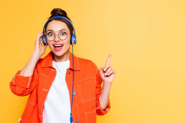 Excited student in headphones showing idea gesture isolated on yellow — Stock Photo