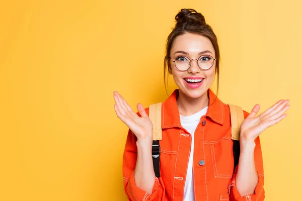 Estudiante feliz en gafas de vista sonriendo mientras está de pie con los brazos abiertos aislados en amarillo - foto de stock