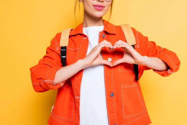 Vue recadrée de l'élève montrant signe cardiaque avec les mains sur fond jaune — Photo de stock