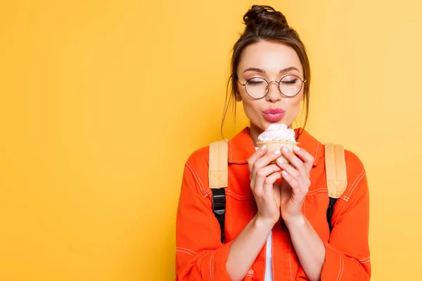 Glückliche Studentin mit geschlossenen Augen mit leckerem Cupcake auf gelbem Hintergrund — Stockfoto