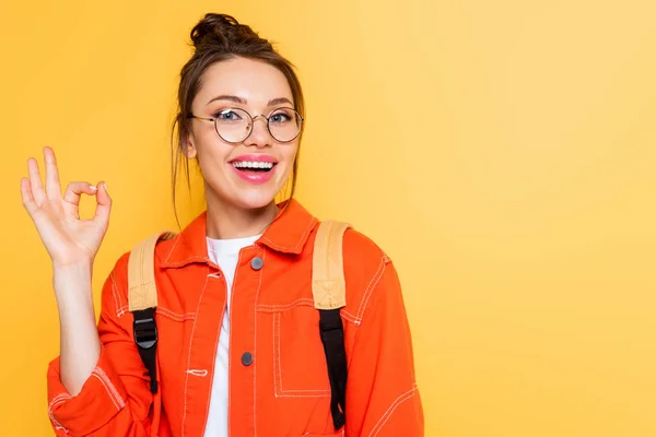 Happy student showing okay gesture while smiling at camera isolated on yellow — Stock Photo