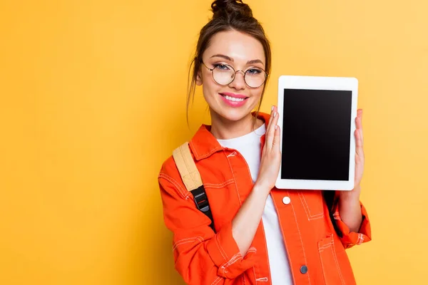 Estudiante alegre en gafas que muestran tableta digital con pantalla en blanco sobre fondo amarillo - foto de stock