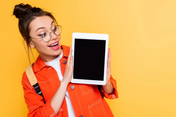 Удивленный студент в очках, показывающих цифровой планшет с чистым экраном изолированы на желтый — стоковое фото
