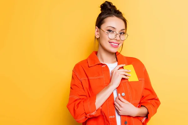Attractive student smiling at camera while taking smartphone out of pocket on yellow background — Stock Photo